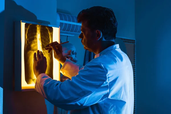 Een arts in een wit gewaad onderzoekt een röntgenfoto van de longen of borst in neonlicht. Een concept over het onderwerp geneeskunde — Stockfoto