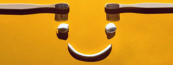 Drewniane szczoteczki do zębów i makaron na żółtym tle. Koncepcja stomatologiczna w postaci śmiesznej twarzy — Zdjęcie stockowe