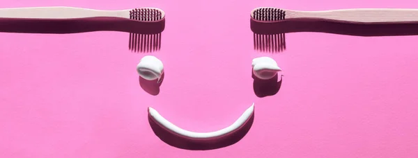 Dřevěné zubní kartáčky a těstoviny na růžovém pozadí. Zubní koncept v podobě legrační tváře — Stock fotografie