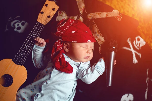 Rock bandanalı bir bebek gitar ve mikrofonla yatıyor.