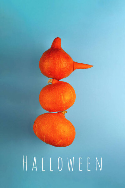 A snowman with a carrot nose of three orange pumpkins on a blue background. Halloween concept.