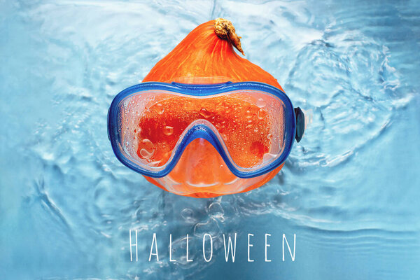 Orange pumpkin swimmer in a mask in blue water. Halloween concept.