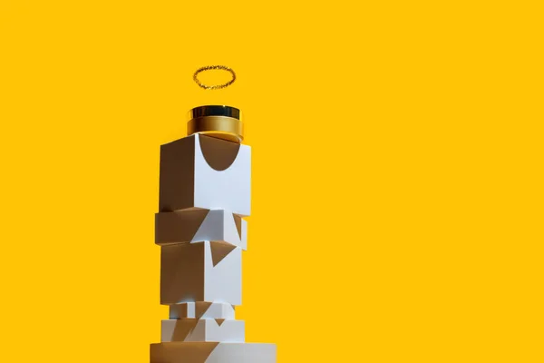 Creme de rosto dourado com um halo como um deus, sobre uma torre de formas geométricas, sobre um fundo amarelo brilhante — Fotografia de Stock