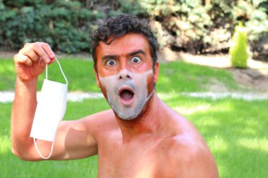 Tıbbi maske şeklinde bronzlaşmış bronz tenli genç adamın yakın plan portresi.