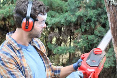 Ormanda testereyle ağaç kesen adam.