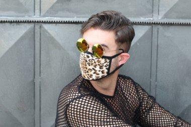Koruyucu tıbbi maskeli, leopar desenli, altın tırnaklı ve sokakta örgü gömlekli şık bir gencin portresi.