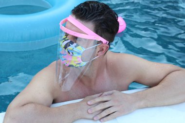 Coronavirus tecridi sırasında yüzme havuzunda tıbbi koruyucu maskeli yakışıklı genç adamın yakın plan portresi.