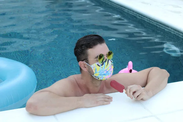 医療用保護マスクのハンサムな若い男のクローズアップ肖像コロナウイルスのロックダウン中にプールでアイスクリーム — ストック写真