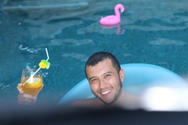 Kokteyl ve yüzme havuzunda gevşeyen şişme tüplü yakışıklı genç adamın yakın plan portresi.