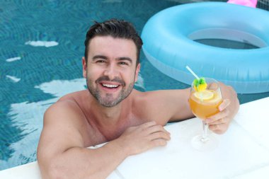 Yüzme havuzunda bir bardak kokteyl içen yakışıklı genç adamın yakın plan portresi.