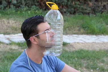 Yeşil Park 'ta tıbbi maske yerine plastik şişeli yakışıklı bir gencin yakın plan portresi. Komedi anlayışı.