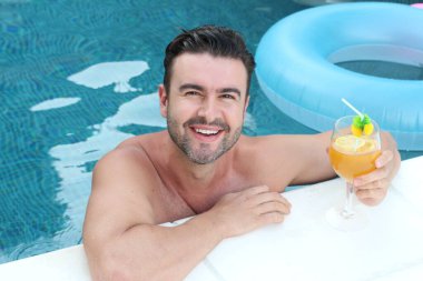 Yüzme havuzunda bir bardak kokteyl içen yakışıklı genç adamın yakın plan portresi.