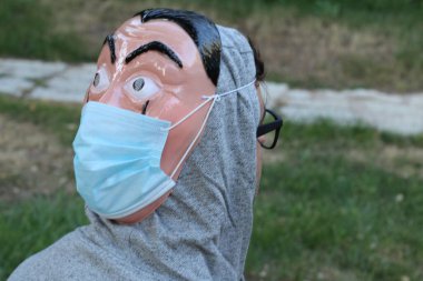 Yeşil Park 'ta korunmak için arka yüzünde plastik maske ve tıbbi maske olan yakışıklı genç adamın yakın plan portresi.