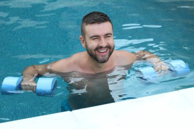 Yüzme havuzunda şişme halterlerle yüzen yakışıklı genç adamın yakın plan portresi.