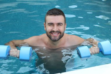Yüzme havuzunda şişme halterlerle yüzen yakışıklı genç adamın yakın plan portresi.