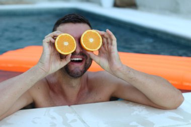 Yüzme havuzunda portakal yarımları tutan yakışıklı genç adamın yakın plan portresi.