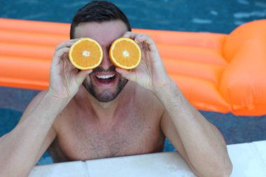 Yüzme havuzunda portakal yarımları tutan yakışıklı genç adamın yakın plan portresi.
