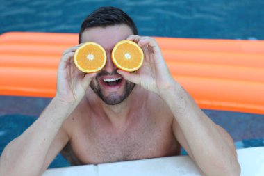 Yüzme havuzunda portakal yarımları tutan yakışıklı genç adamın yakın plan portresi.