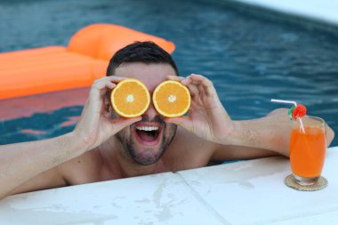Yüzme havuzunda portakal yarımları tutan yakışıklı genç adamın yakın plan portresi.