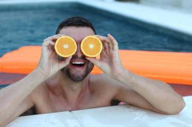 Yüzme havuzunda portakal yarımları tutan yakışıklı genç adamın yakın plan portresi.