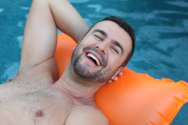 Yüzme havuzunda şişme yatakta yüzen yakışıklı genç adamın yakın plan portresi.