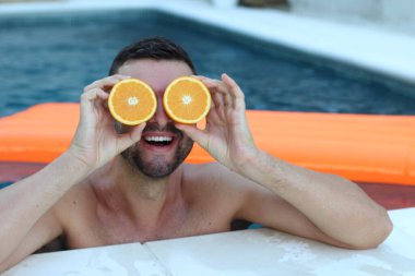 Yüzme havuzunda portakal yarımları tutan yakışıklı genç adamın yakın plan portresi.