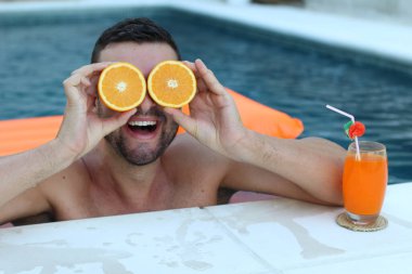 Yüzme havuzunda portakal yarımları tutan yakışıklı genç adamın yakın plan portresi.