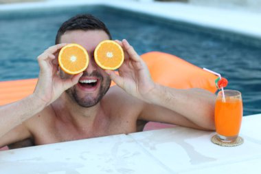 Yüzme havuzunda portakal yarımları tutan yakışıklı genç adamın yakın plan portresi.