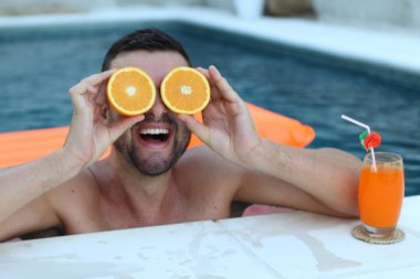 Yüzme havuzunda portakal yarımları tutan yakışıklı genç adamın yakın plan portresi.