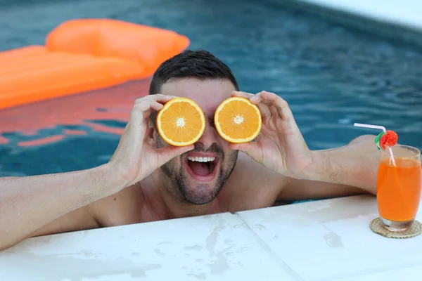 在游泳池里 年轻帅小伙拿着一半橙子站在眼边的特写 — 图库照片