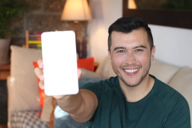 Boş akıllı telefon tutan yakışıklı genç adamın yakın plan portresi ve kamerada gösteriliyor.