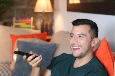 Evdeki kanepede oturan uzaktan kumandalı yakışıklı genç adamın yakın plan portresi.