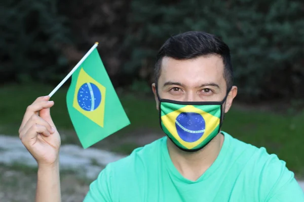 portrait of young man with protection mask and Brazilian flag on nature
