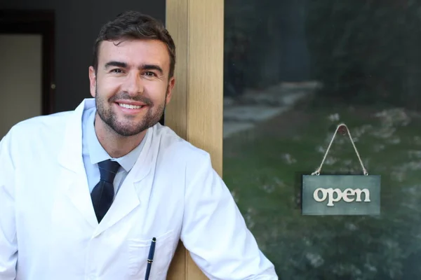 close-up portrait of handsome young doctor in front of glass door with open sign board