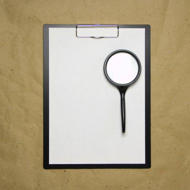 Üzerinde bej el işi kağıdının üzerinde büyüteç bulunan beyaz A4 formatlı bir tablet. Analiz anlayışı, çalışma, özenli çalışma. Metnin ve tasarımın için boş yeri olan stok fotoğrafı.