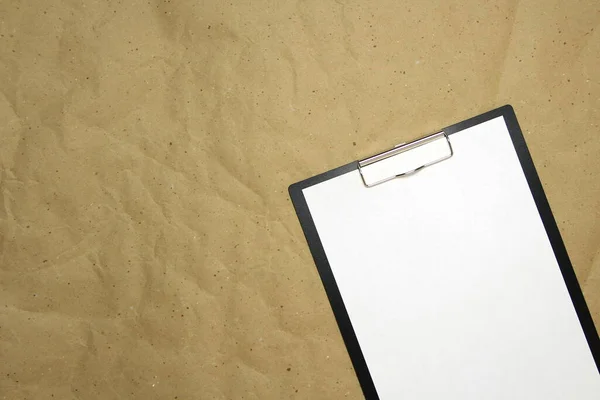 A tablet with a white sheet of A4 format on a beige craft paper. Concept of new opportunities, ideas, undertakings, innovations. Stock photo with empty place for your text and design.