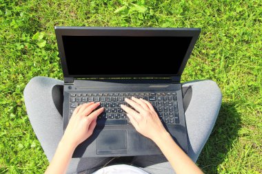 Kız çimenlikteki yeşil çimlerin üzerinde oturuyor, kucağında siyah bir dizüstü bilgisayar tutuyor. Dizüstü bilgisayarı kapat..