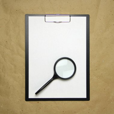 Üzerinde bej el işi kağıdının üzerinde büyüteç bulunan beyaz A4 formatlı bir tablet. Analiz anlayışı, çalışma, özenli çalışma. Metnin ve tasarımın için boş yeri olan stok fotoğrafı.