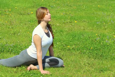 Avrupa görünümlü genç bir kadın yaz doğasında yoga yapıyor. Güvercin pozunda oturan kadın, eka pada rajakapotasana. Metin ve tasarım için boş alanı olan web ve yazıcı için yüksek kaliteli fotoğraf.