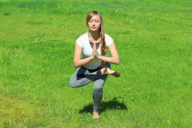 Avrupa görünümlü genç bir kadın yaz doğasında yoga yapıyor. Kartal pozu veren kadın, Garudasana. Metin ve tasarım için boş alanı olan web ve yazıcı için yüksek kaliteli fotoğraf.