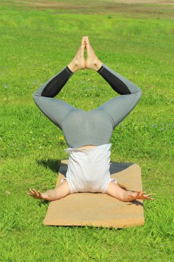 Avrupa görünümlü genç bir kadın yaz doğasında yoga yapıyor. Kadın kapalı açılı amuda kalkıyor, badhakona shirshasana. Metin ve tasarım için boş alanı olan web ve yazıcı için yüksek kaliteli fotoğraf.
