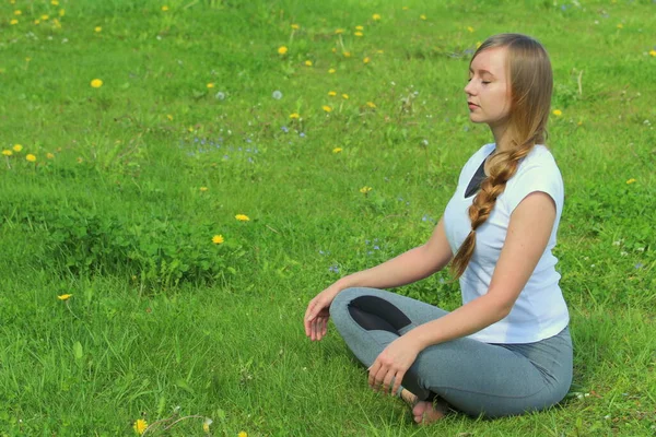Avrupa görünümlü genç bir kadın yaz doğasında yoga yapıyor. Kolay poz veren bir kadın, sukhasana. Metin ve tasarım için boş alanı olan web ve yazıcı için yüksek kaliteli fotoğraf.