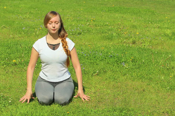 Young woman of European appearance does yoga in summer nature. Woman sitting in hero pose, virasana. High quality photo for web and print with empty space for text and design.