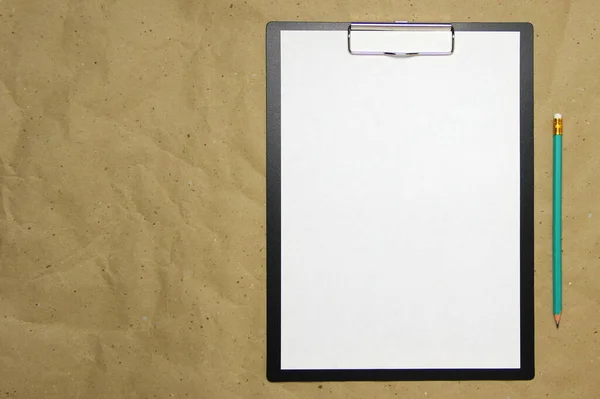Una tableta con una hoja blanca de formato A4 sobre un papel artesanal beige. —  Fotos de Stock