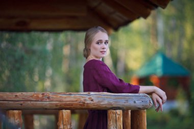 Bordo elbiseli bir kız asılmış ahşap bir köprüde yürüyor. Gülümseyen sarışın