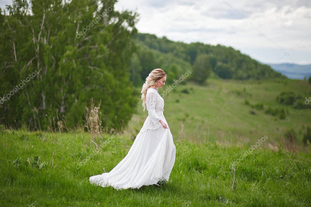 the bride walks in the field against the backdrop of the mountains, a photo shoot in Altai, a portrait of the bride, a girl in a white dress in the style of boho
