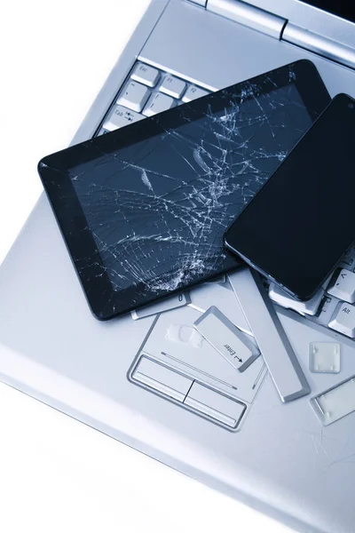 A silver laptop with a broken keyboard, tablet with a cracked display and black phone. A close-up picture of part of broken laptop and cracked screen on a tablet.