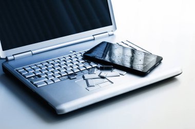 Kırık klavyeye sahip gümüş bir dizüstü bilgisayar, kırık ekranlı tablet ve siyah telefon. Tablette bozuk dizüstü bilgisayar ve kırık ekranın bir kısmının yakın çekim resmi.