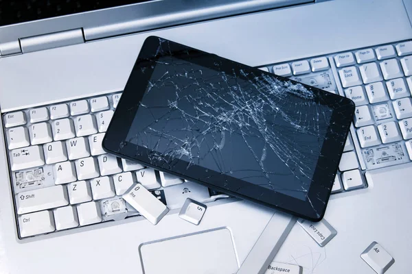 Un laptop argentato con tastiera rotta, tablet con display incrinato e telefono nero. Un primo piano immagine di parte del computer portatile rotto e schermo rotto su un tablet . — Foto Stock