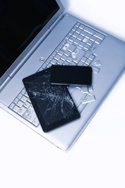 Kırık klavyeye sahip gümüş bir dizüstü bilgisayar, kırık ekranlı tablet ve siyah telefon. Tablette bozuk dizüstü bilgisayar ve kırık ekranın bir kısmının yakın çekim resmi.